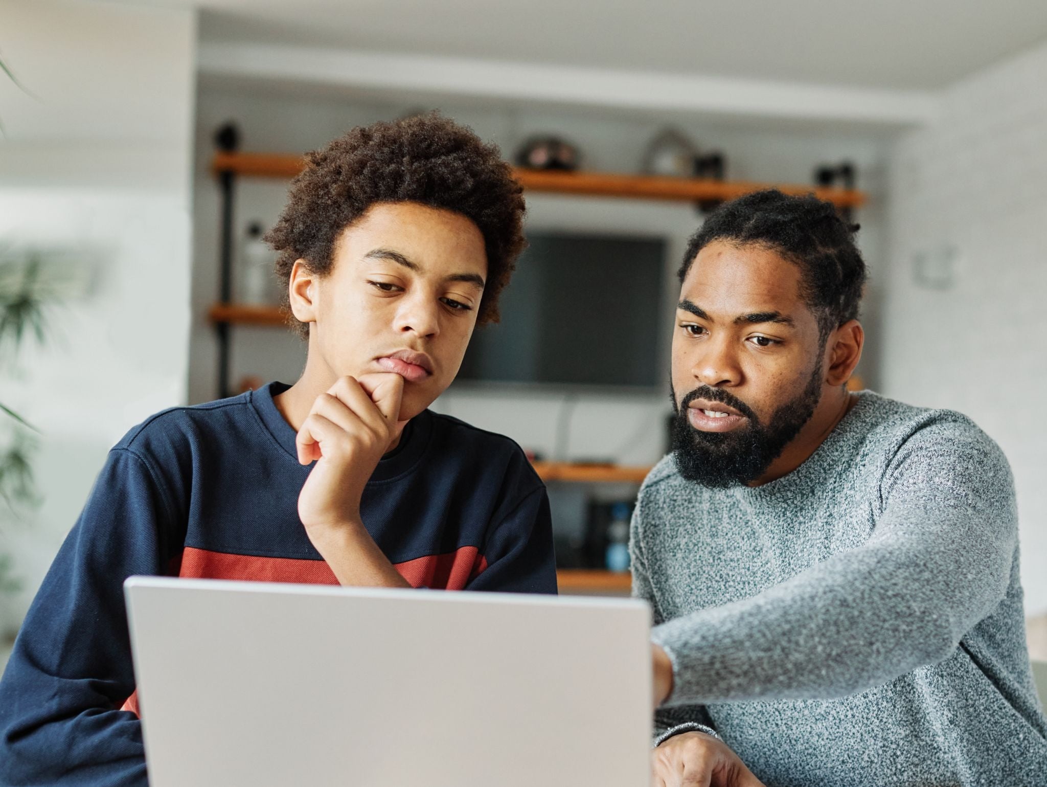 Adult and child focused on a laptop screen, adult pointing.