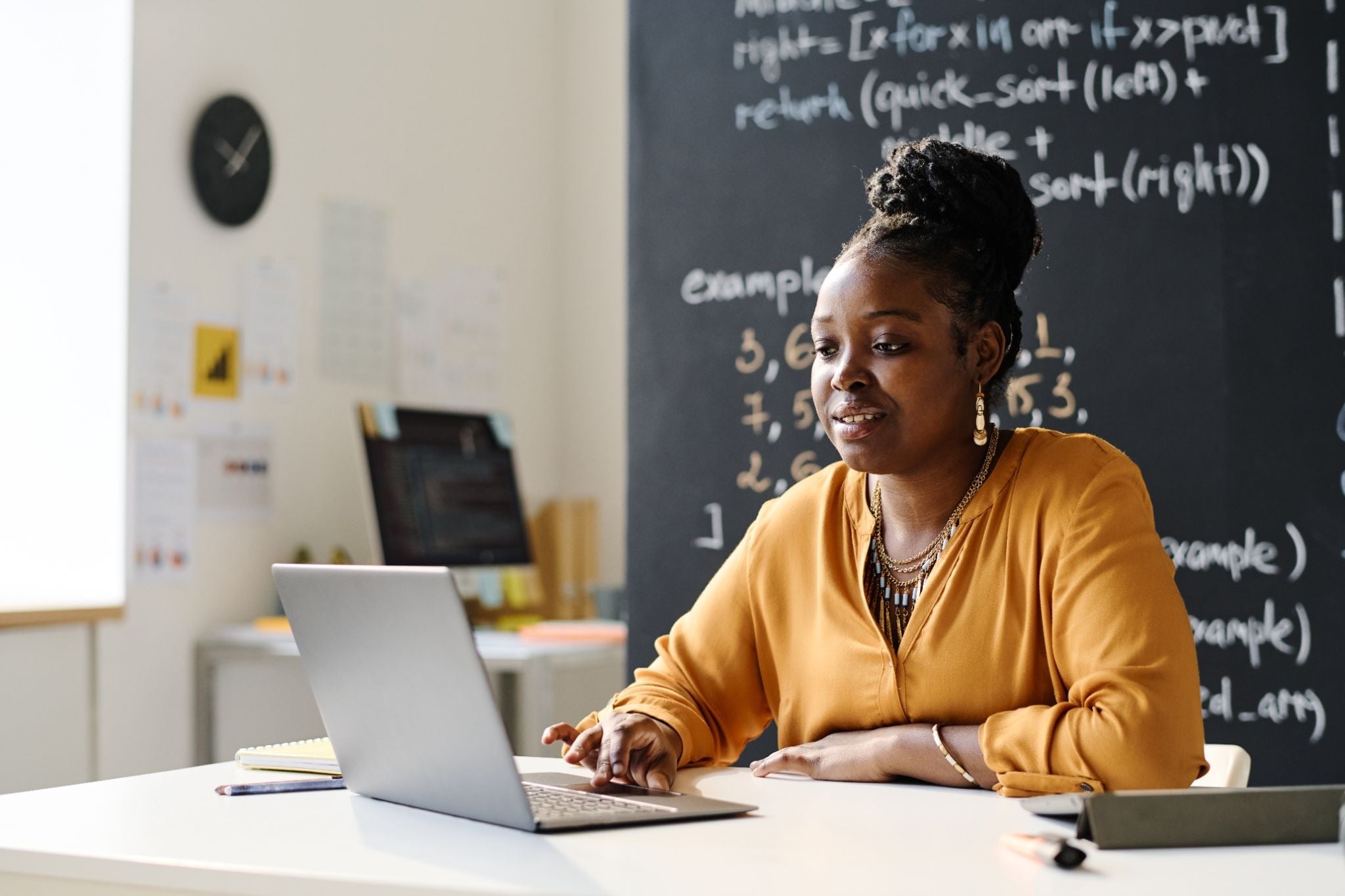 Adult using a laptop in a classroom with a blackboard behind them.