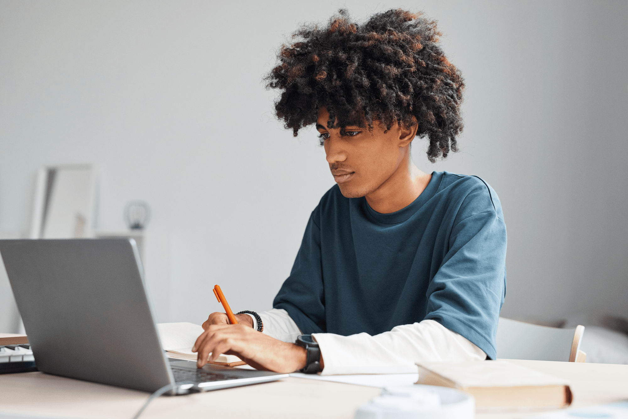 Young adult student working on laptop and writing in a notebook.