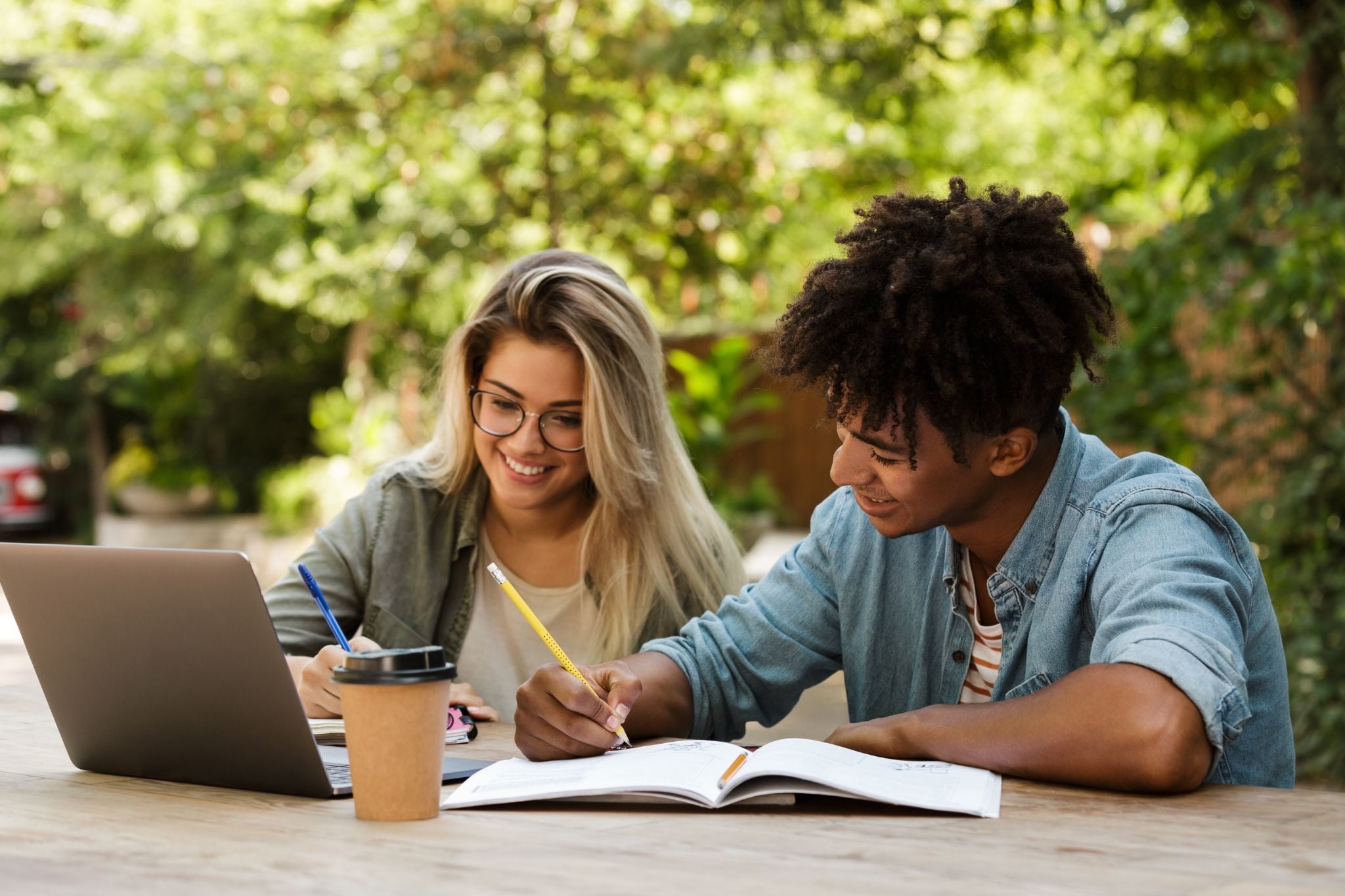 Two adults studying outdoors with a laptop and notebooks.